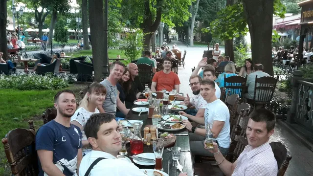 

Smiling crowd gathers around table with tree and tableware, dressed in