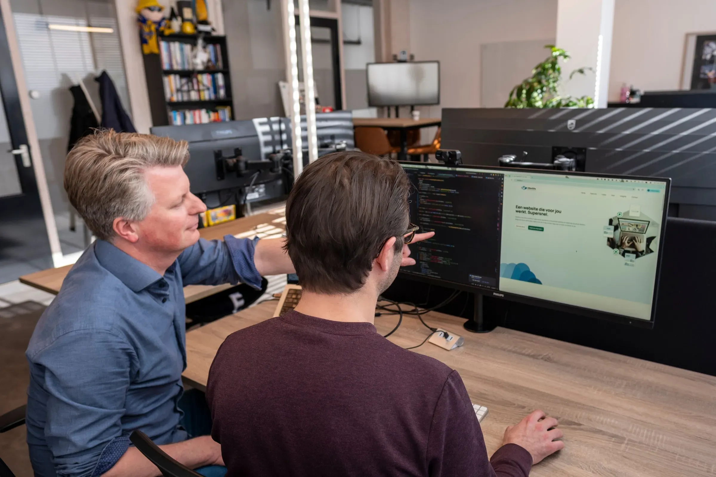 Twee collega’s van ZEN Software kijken samen naar een scherm met code en een ontwerp, aan een bureau op kantoor in Alkmaar.